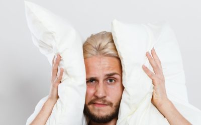 Man holding two white pillows, looking frustrated, emphasizing the importance of washing pillows for better sleep, relevant to Redbud Laundry Company's advice on laundry hygiene.