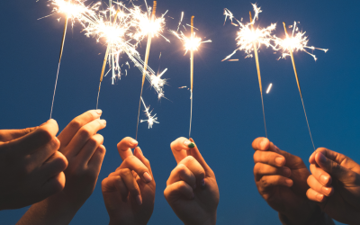 Hands holding sparklers against a dark sky, celebrating the Fourth of July, symbolizing festive summer gatherings and outdoor celebrations.